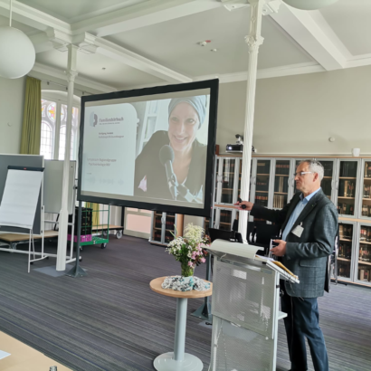 Sprecher steht am Stehpult. Im hintergrund läuft eine Präsentation.